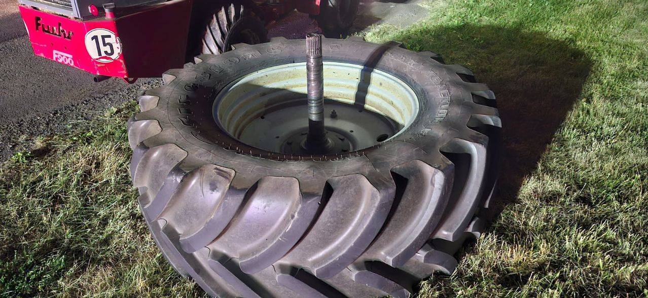 Eine Nahaufnahme eines großen Traktorreifens mit einem Metallachsen, der aus seinem Zentrum ragt, auf Gras liegend.