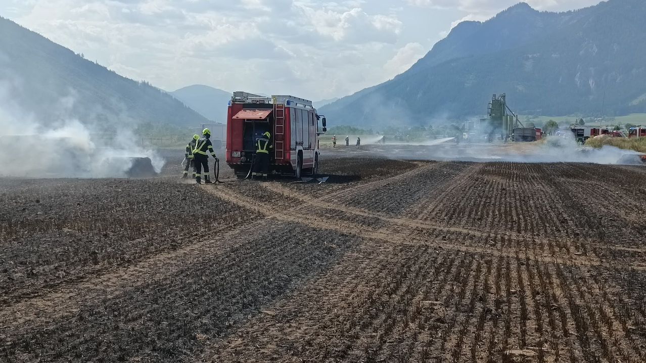 Firefighters are using a fire truck to extinguish a fire in a field with mountains in the background.