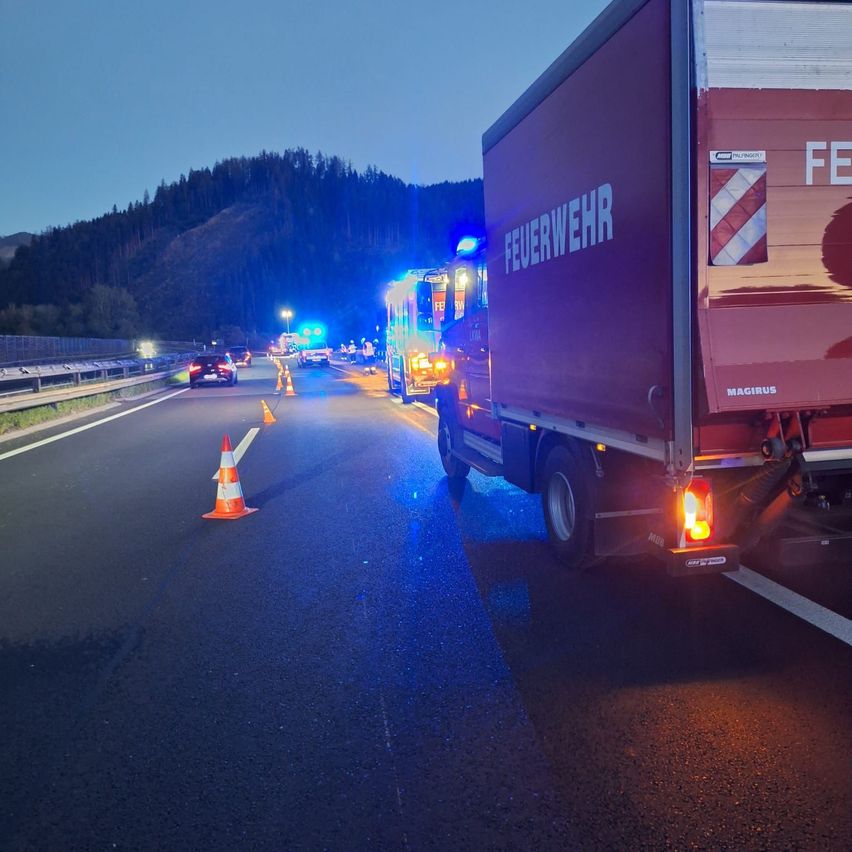 Ein Feuerwehrfahrzeug ist am Straßenrand geparkt, die Notfallleuchten sind eingeschaltet. Ein Verkehrskegel ist auf der Straße platziert.