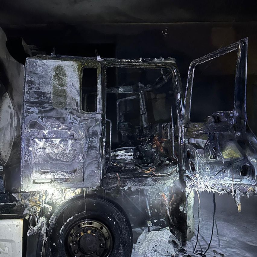 Ein verbranntes Fahrzeug mit offenen Türen, durch Feuer beschädigt, liegt auf dem Boden. Der Innenraum ist verkohlt, und Rauch ist noch sichtbar.