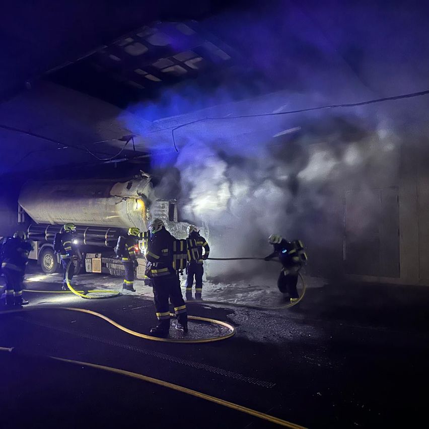 Feuerwehrleute löschen einen Brand in einem Kraftstofflager. Sie verwenden einen Schlauch, um Wasser auf die Flammen zu spritzen. Rauch und Dampf kommen aus der Anlage.