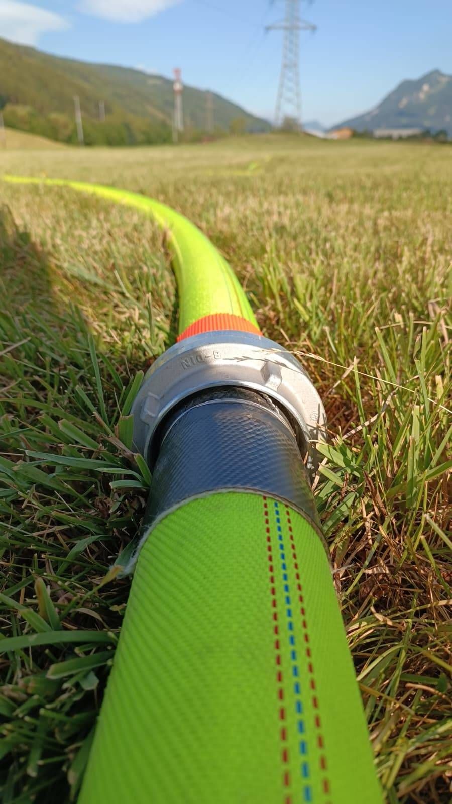 A close-up view of a green and blue hose with red and blue stripes on a grassy field.