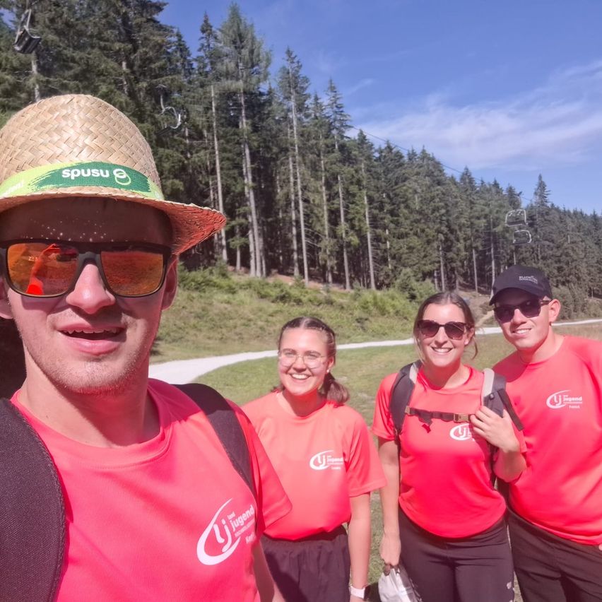 Vier Personen in roten Shirts lächeln und posieren für ein Foto in einem Grasbereich mit Waldhintergrund.