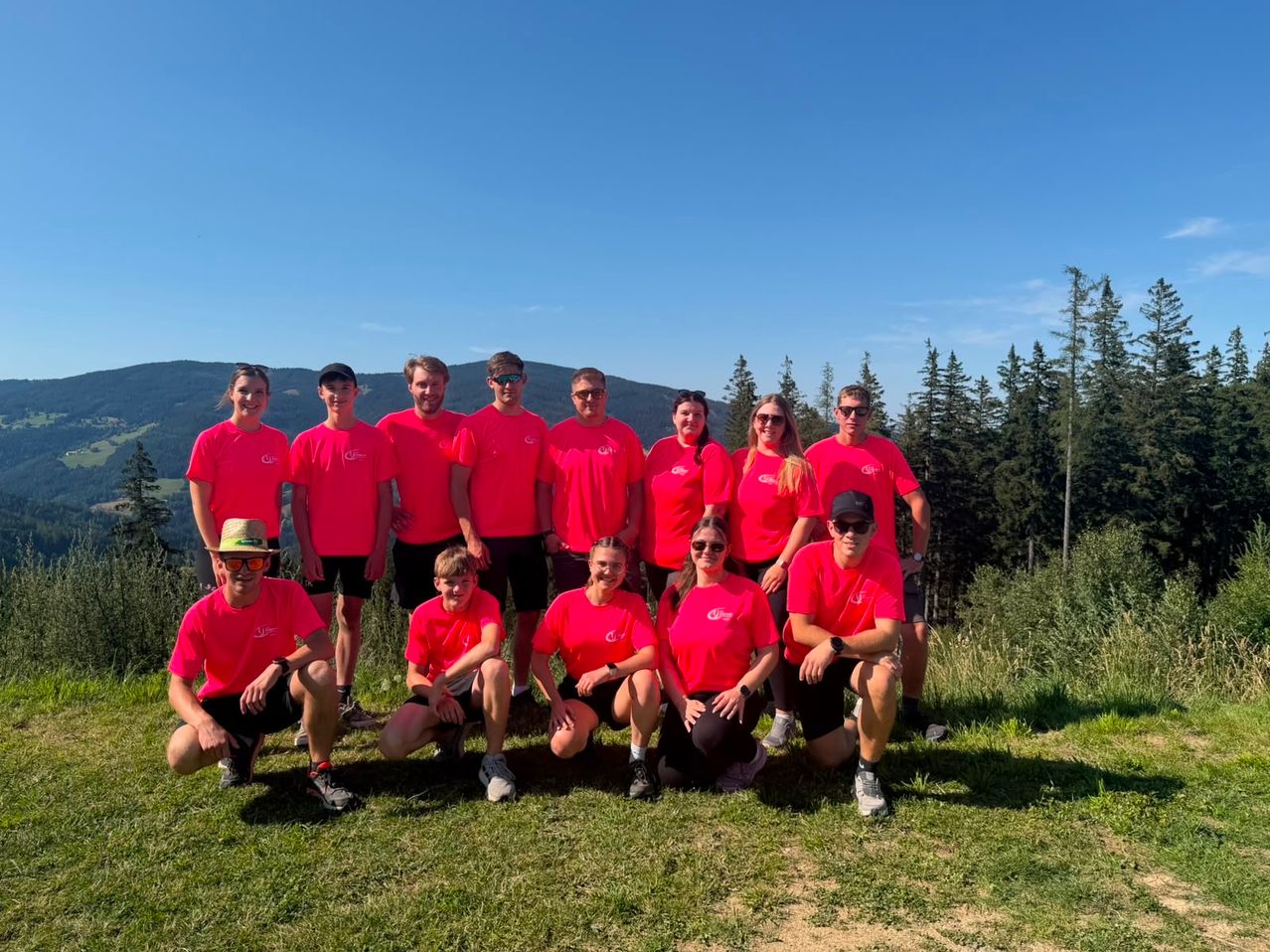 Gruppe in pinken T-Shirts in der Steiermark vor bewaldeten Hügeln