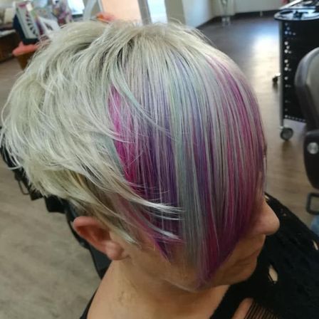 Eine Frau mit kurzen blonden Haaren und leuchtenden rosa und lila Strähnen schaut in einem Salon nach unten.