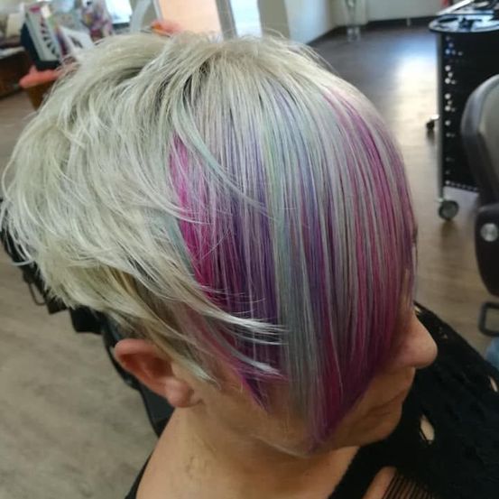 Eine Frau mit kurzen blonden Haaren und leuchtenden rosa und lila Strähnen schaut in einem Salon nach unten.