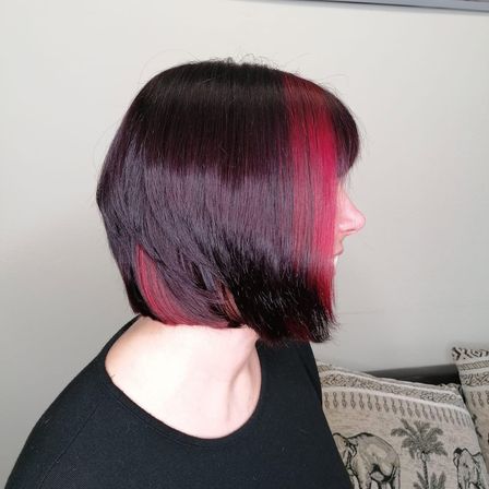 Eine Frau mit kurzen Haaren, die von dunkellila zu leuchtend pink verlaufen, schaut zur Seite.