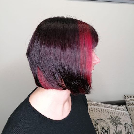 Eine Frau mit kurzen Haaren, die von dunkellila zu leuchtend pink verlaufen, schaut zur Seite.