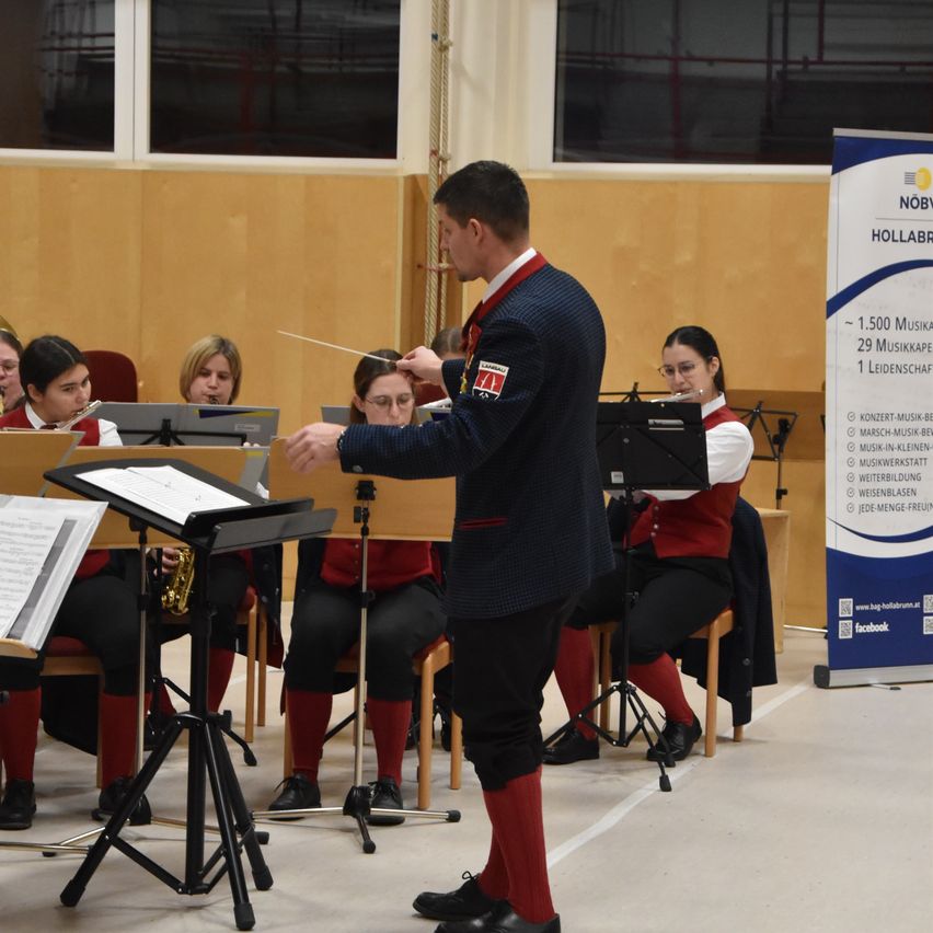 Ein Dirigent leitet eine Brass Band mit mehreren Musikern, die Instrumente spielen. Der Hintergrund zeigt eine Holzwand.