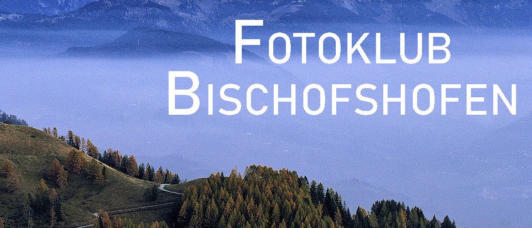 Ein Panoramablick auf eine Bergregion mit schneebedeckten Gipfeln und einer friedlichen Atmosphäre. Im Vordergrund zeigt sich üppiges Grün und eine kurvenreiche Straße.