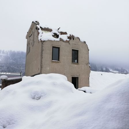 Ein altes, beschädigtes Gebäude, das in Schnee bedeckt ist, steht inmitten einer verschneiten Landschaft mit Bäumen in der Ferne.