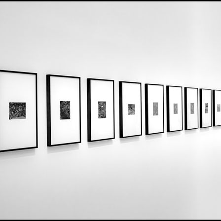 Eine Reihe schwarz-weißer gerahmter Fotografien ist an einer weißen Wand montiert. Die Bilder sind in einer geraden Linie angeordnet.