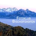 Eine Bergkette mit schneebedeckten Gipfeln und einem nebligen Tal, beschriftet mit 'Fotokl Bischofsh', umgeben von einem üppigen Wald mit Herbstlaub.
