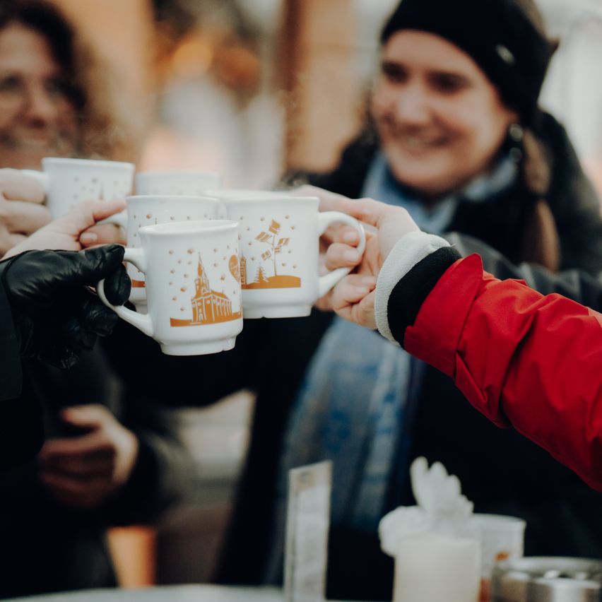 Mehrere Menschen in Winterkleidung halten Tassen mit Schloss-Design und stoßen möglicherweise mit ihnen an.