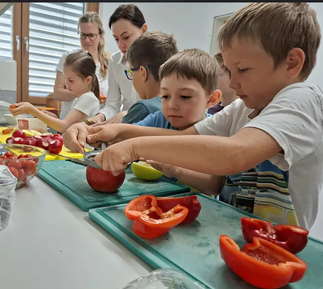 Eine Gruppe von Kindern bereitet unter Aufsicht roter Paprika auf einem Küchentisch zu.