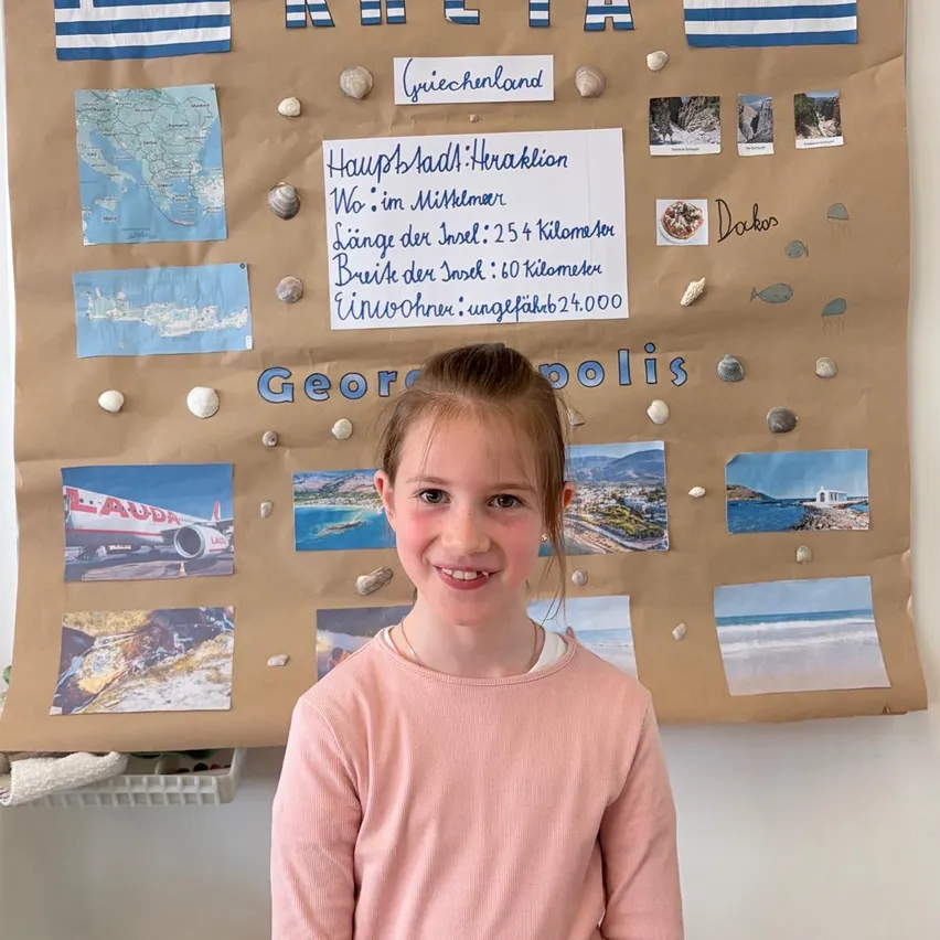 Ein Mädchen posiert vor einer Pinnwand über Kreta, Griechenland, mit Bildern, Muscheln und Texten über die Hauptstadt der Insel, die Entfernung von Athen und die Einwohnerzahl.