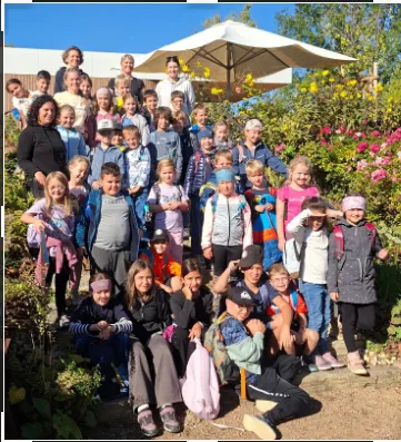 Eine Gruppe von Kindern und Erwachsenen posiert für ein Foto in einem Garten mit Blumen und einem weißen Schirm im Hintergrund.