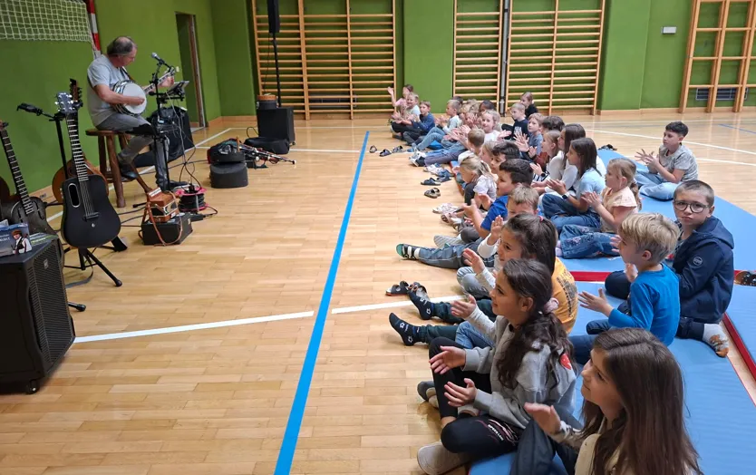 Ein Mann spielt ein Banjo vor einer Gruppe von Kindern, die auf dem Boden sitzen.