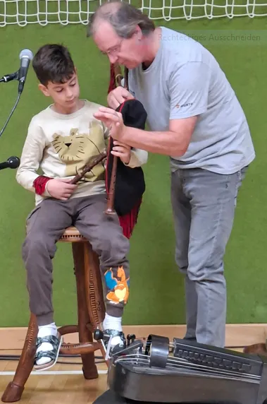Ein Mann hilft einem jungen Jungen, ein Musikinstrument, möglicherweise eine Blockflöte, in einer Klassenzimmerumgebung zu justieren.