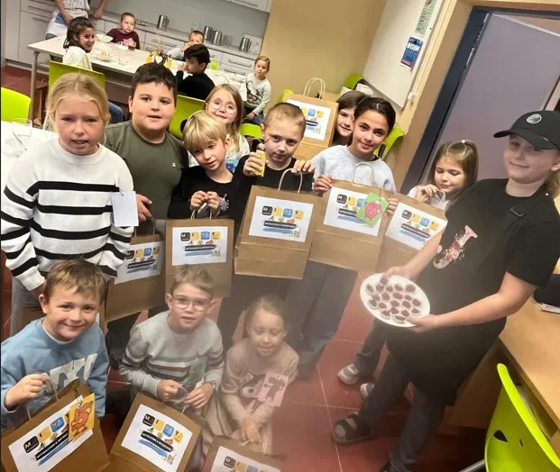 Eine Gruppe von Kindern im Klassenzimmer, die Papiertüten mit Zeichnungen halten.