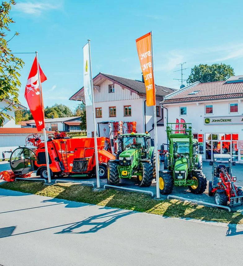 Ein John Deere-Händler mit mehreren Traktoren, die draußen geparkt sind, einschließlich eines roten mit einer weißen Flagge und eines orangefarbenen mit einer gelben Flagge.