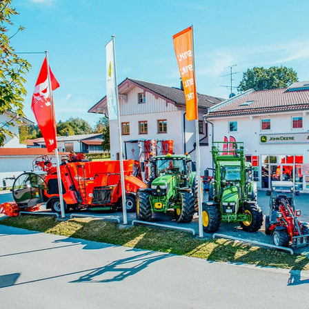 Ein John Deere-Händler mit mehreren Traktoren, die draußen geparkt sind, einschließlich eines roten mit einer weißen Flagge und eines orangefarbenen mit einer gelben Flagge.
