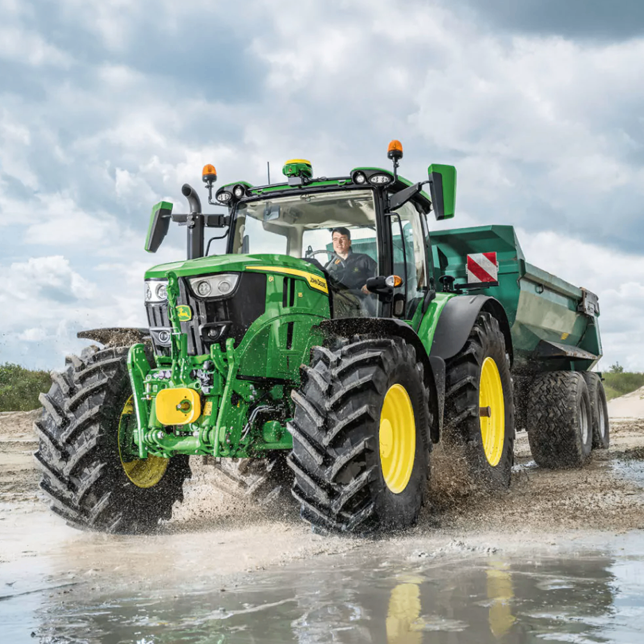 Ein grüner Traktor mit gelber Front und einem großen Anhänger fährt durch ein schlammiges Feld.