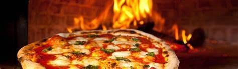 Eine Pizza mit geschmolzenem Käse, Tomatensoße und Kräutern wird in einem Holzofen gebacken. Die hellen Flammen des Ofens beleuchten die Pizza.