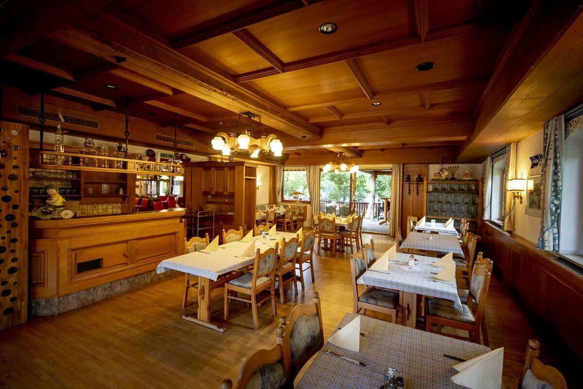 Ein leeres, holzmöbliertes Restaurant mit hohen Decken und Fenstern, die zu einem Außenbereich führen.