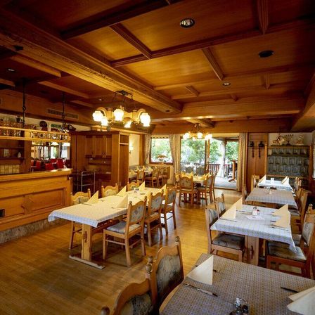 Ein leeres, holzmöbliertes Restaurant mit hohen Decken und Fenstern, die zu einem Außenbereich führen.