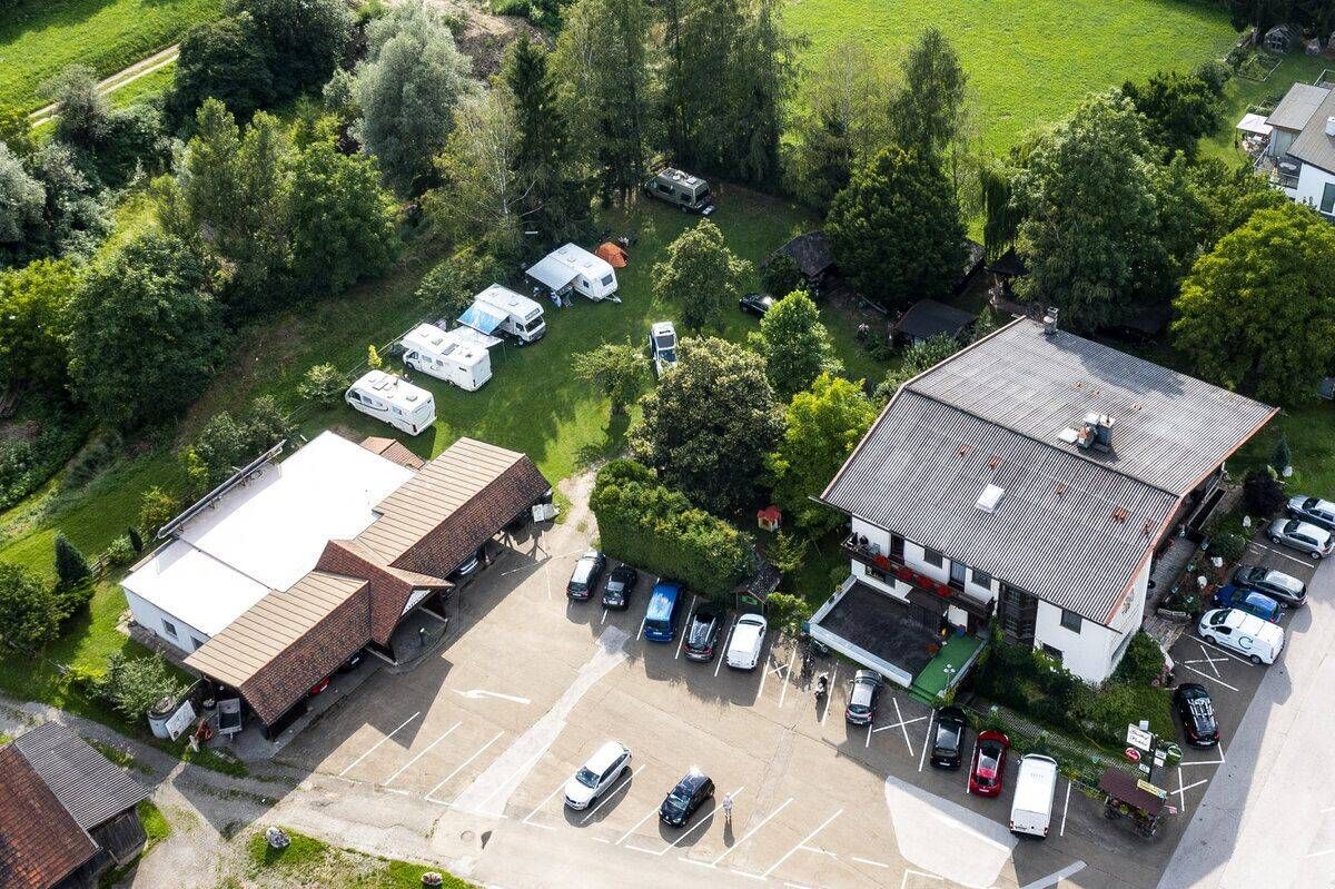 Eine Draufsicht auf einen Campingplatz mit mehreren geparkten Wohnmobilen, einem Gebäude mit braunem Dach und einem Parkplatz mit mehreren Autos und Lieferwagen.