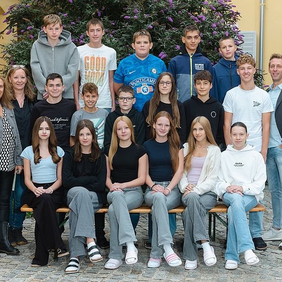 Eine Gruppe von Schülern und zwei Lehrern posiert für ein Foto vor einem Gebäude mit lila Blumen.