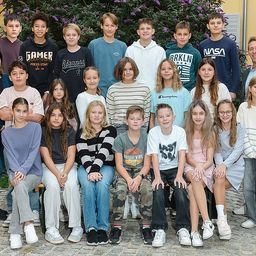 Eine Gruppe von Schülern und zwei Lehrern posiert für ein Foto vor einem Gebäude mit gelber Wand und weißen Fensterläden.