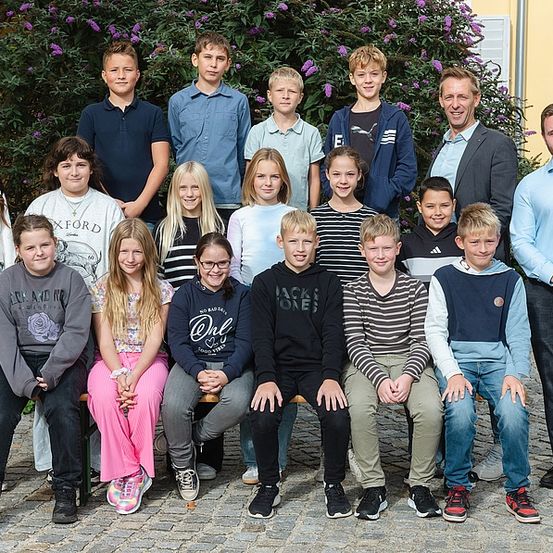 Eine Gruppe junger Menschen und zwei Männer posieren für ein Foto vor einem grünen Busch.