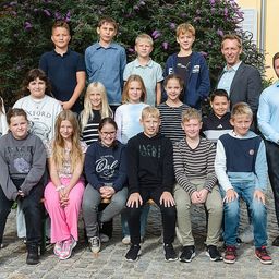 Eine Gruppe junger Menschen und zwei Männer posieren für ein Foto vor einem grünen Busch.