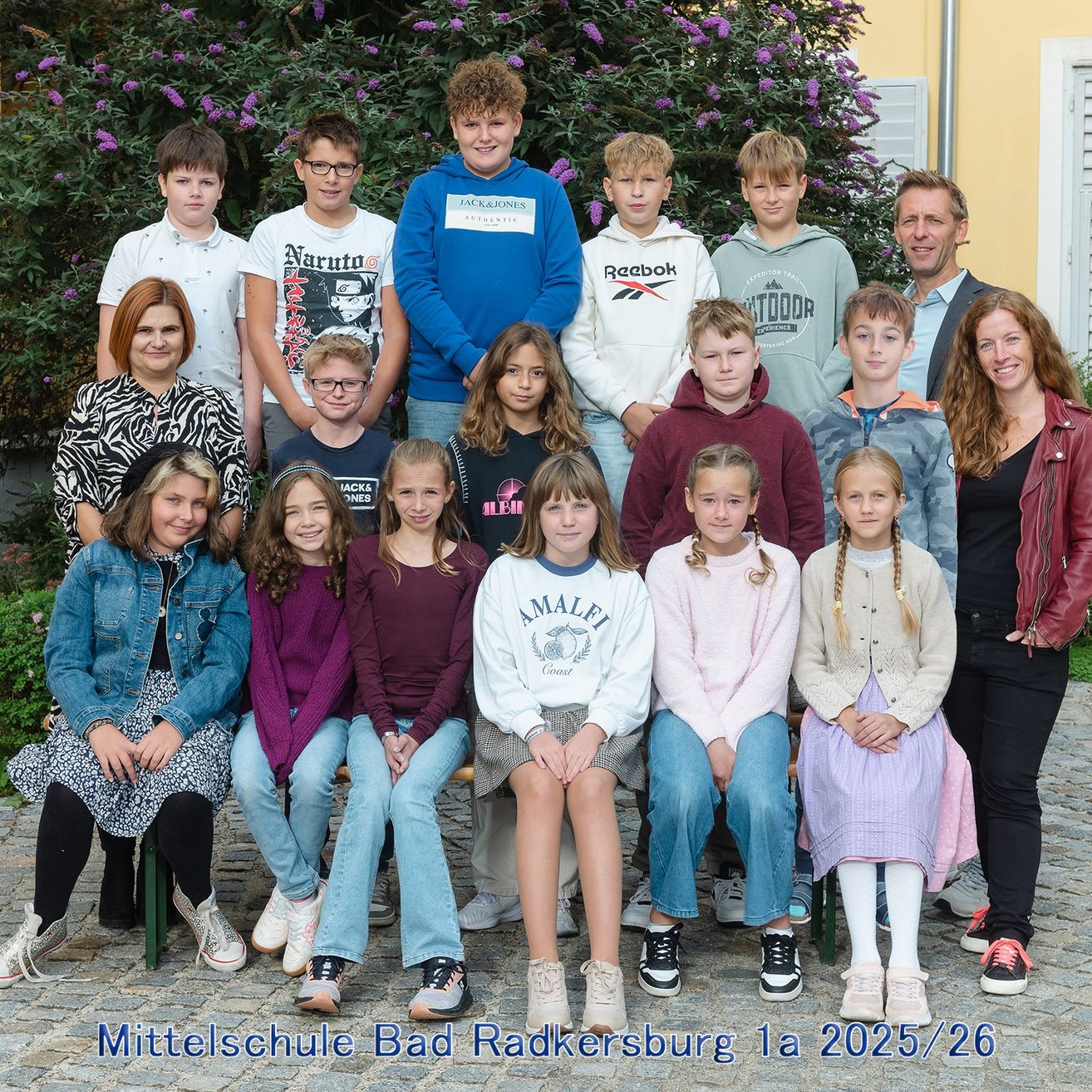 Ein Gruppenfoto der Schüler und Lehrer der Mittelschule Bad Radkersburg, aufgenommen im Jahr 2025/26. Die Schüler sitzen und stehen vor einem grünen Busch.
