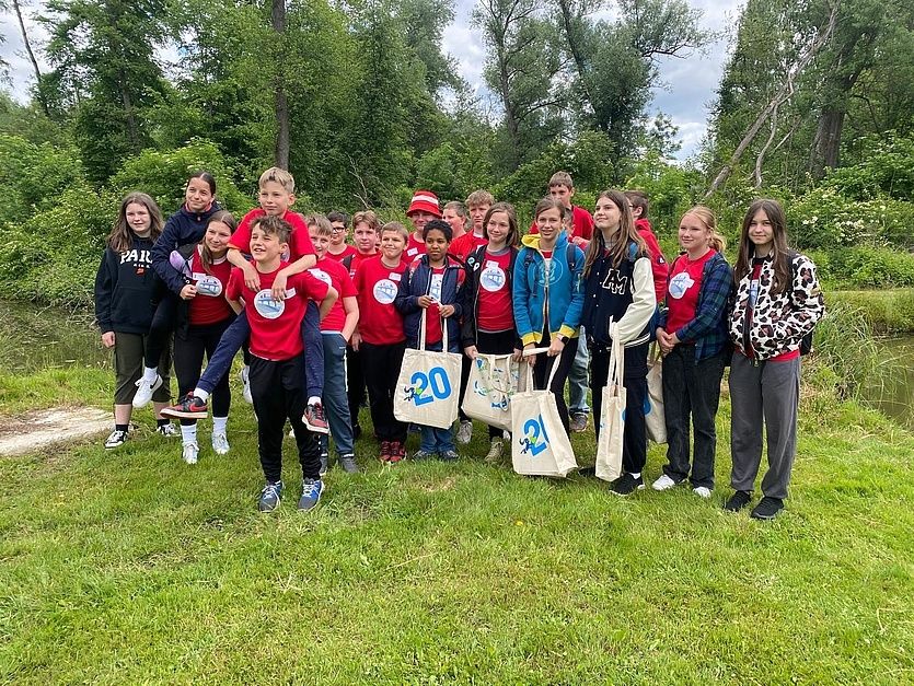 Eine Gruppe junger Menschen in roten Shirts posiert für ein Foto in einem Park mit Taschen.