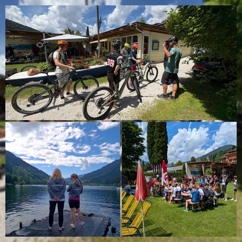 A group of people are on a mountain biking trip. Some ride bikes while others relax on benches and around tables. They are in a scenic area with mountains and a lake.