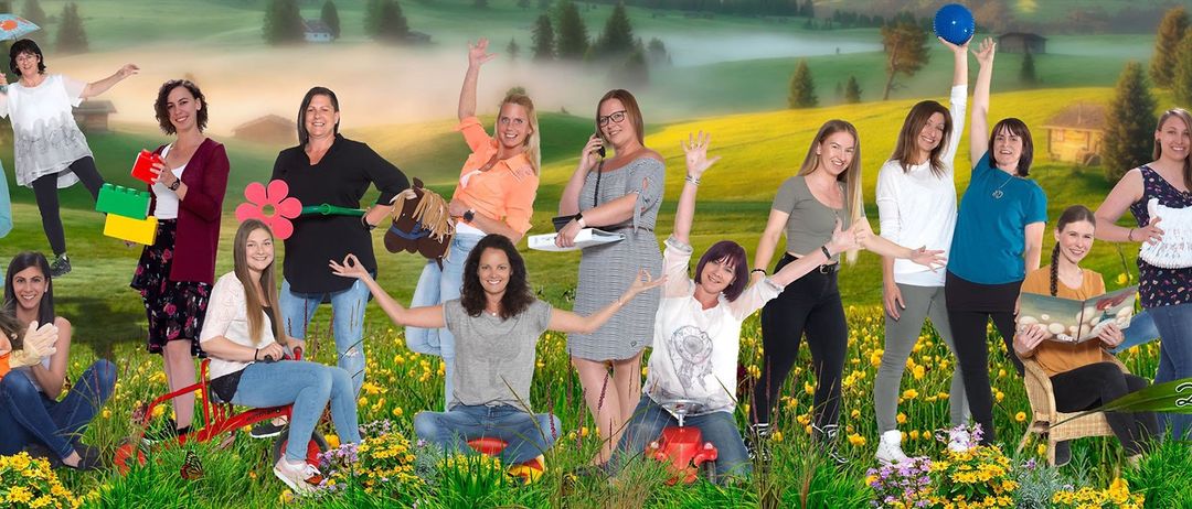 Sieben Frauen posieren für ein Foto auf einem Feld. Sie haben ihre Hände erhoben. Eine Frau hält ein Spielzeugpferd. Sie alle lächeln. Der Hintergrund ist ein grasbewachsenes Feld.