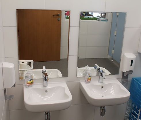 Zwei Waschbecken mit Wasserhähnen und Seifenspendern befinden sich in einem Badezimmer. Ein Spiegel reflektiert das Badezimmer.