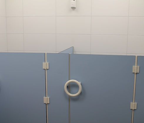 Eine Nahaufnahme einer öffentlichen Toilettenkabine mit blauen Wänden, weißen Fliesen und einem weißen Griff.