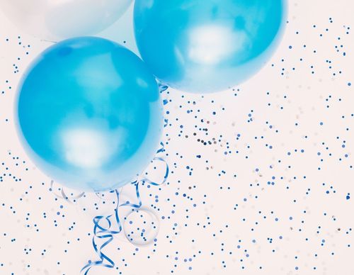 Drei blaue Luftballons, einer mit einer Schleife, schweben vor einem weißen Hintergrund, der mit blauem und silbernem Konfetti bedeckt ist.