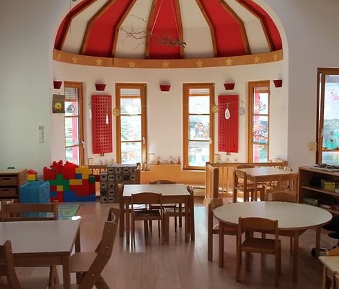 Ein kreisförmiger Raum mit Holzböden und Tischen. Rote Sterne schmücken die kuppelförmige Decke. Fenster sind symmetrisch um den Raum herum angeordnet, und Regale halten verschiedene Gegenstände.