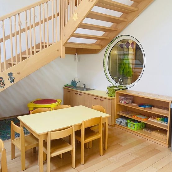 Ein kleiner Essbereich mit einem Holztisch und Stühlen, einer Holztreppe und einem runden Spiegel. Es verfügt über ein Waschbecken und Schränke.
