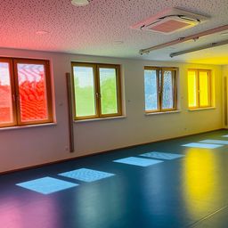 Ein leerer Raum mit blauem und gelbem Boden. Drei Fenster mit verschiedenen Farben sind an der Wand. Ein gelbes Quadrat ist auf dem Boden.