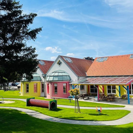 Ein farbenfrohes Gebäude mit Spielplatz und Picknickbereich davor, unter einem klaren blauen Himmel.