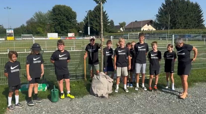 Eine Gruppe junger Jungen und Männer in passenden Nike-Shirts posiert für ein Foto vor einem Zaun mit einem Baum.