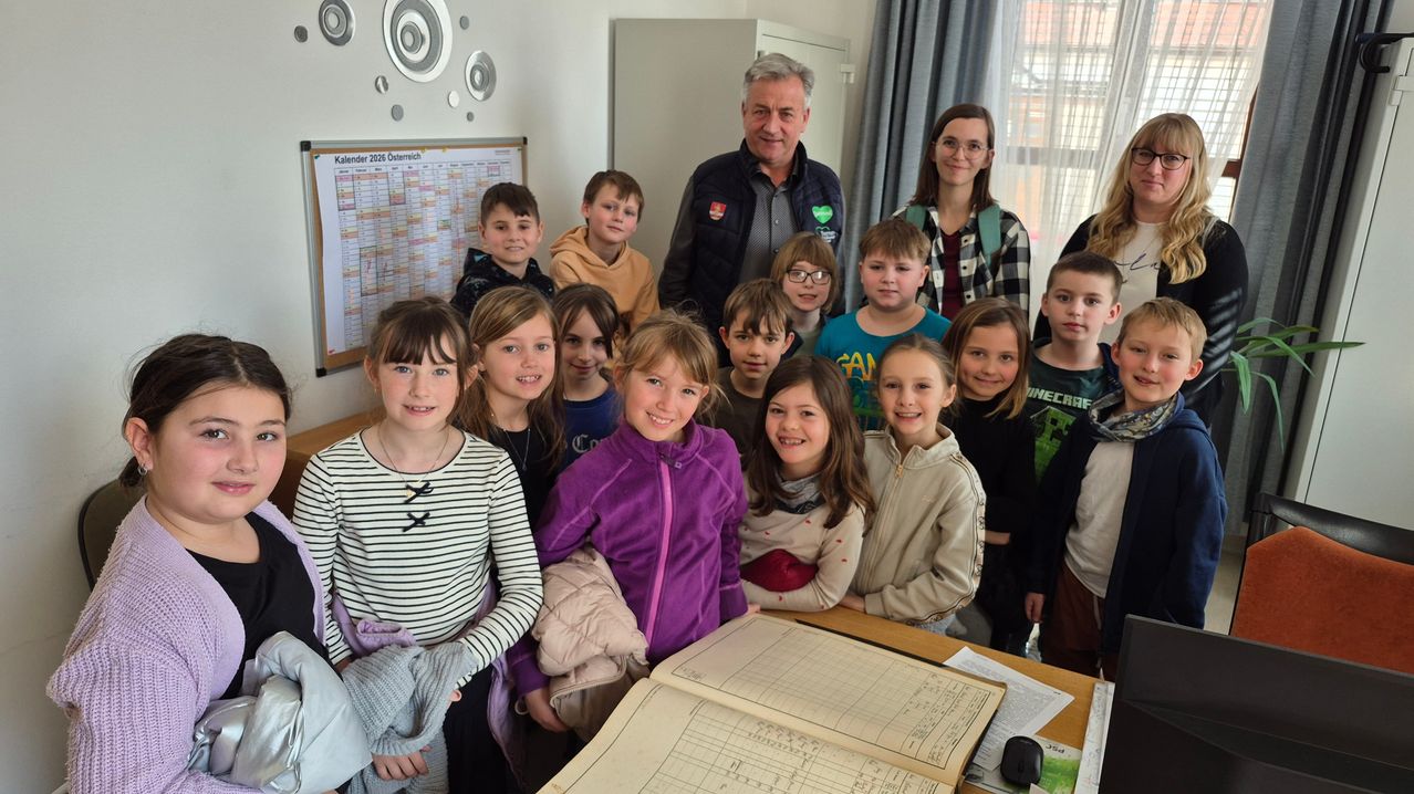 Eine Gruppe von Kindern und Erwachsenen posiert für ein Foto in einem Klassenzimmer mit einem Kalender an der Wand.