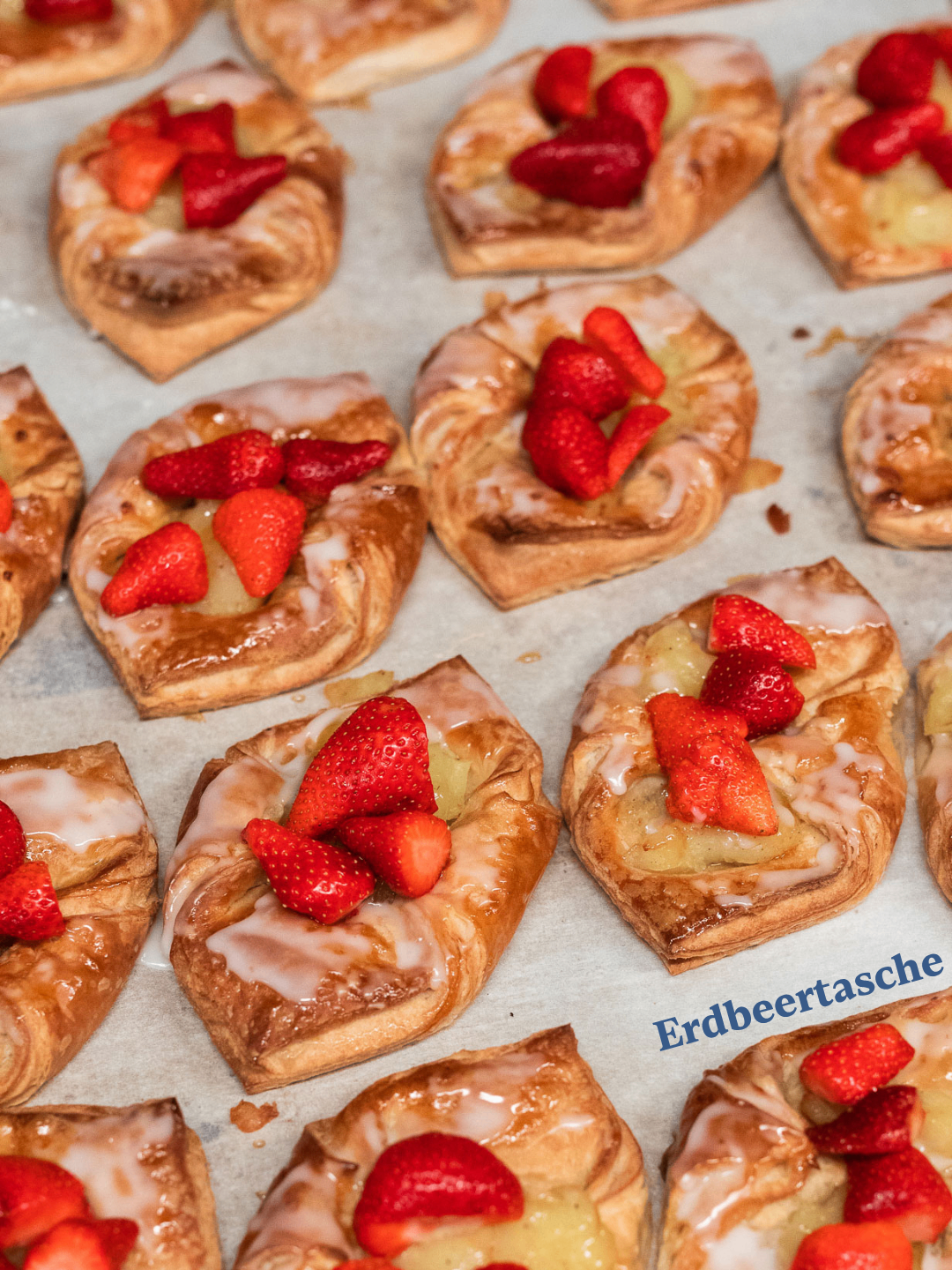 Nahaufnahme von mehreren herzförmigen Gebäckstücken mit Himbeeren und Zuckerguss obenauf. Die Gebäckstücke sind auf einer weißen Oberfläche platziert.