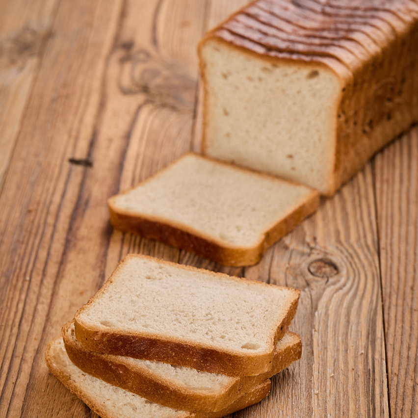 Ein Laib Weißbrot mit drei herausgeschnittenen Scheiben, auf einer Holzoberfläche. Das Brot hat eine goldbraune Kruste und ein weiches, helles Inneres.